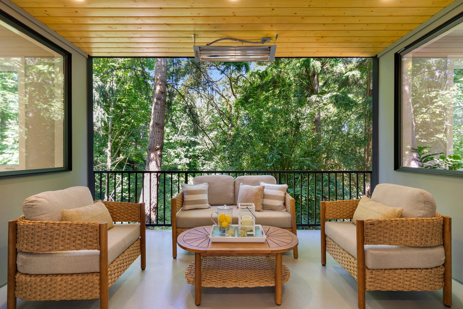 Covered outdoor living area with overhead heater and wooded backdrop.setting.